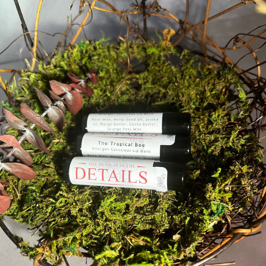 Three tubes of the tropical bee lip balm on a bed of moss. next to a red tie frond